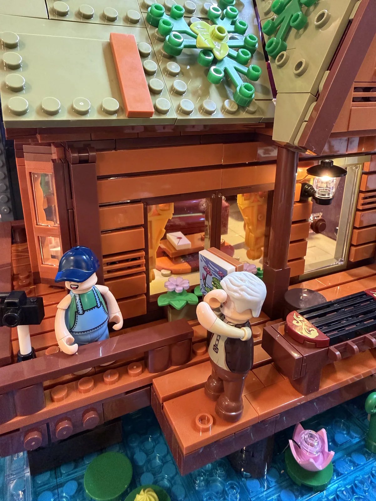 Lumibricks 10010 Waterfall Cabin — both minifigures on the deck with camera, frog painting and lantern lit