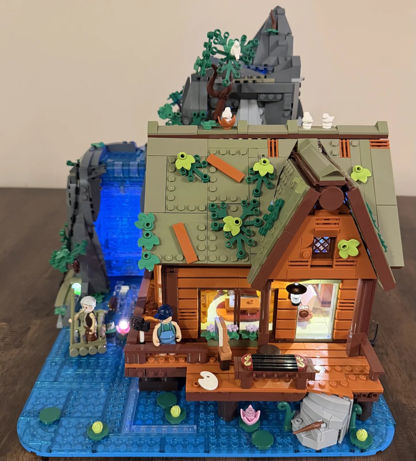 Lumibricks 10010 Waterfall Cabin — finished build lit, front view with raft and glowing waterfall