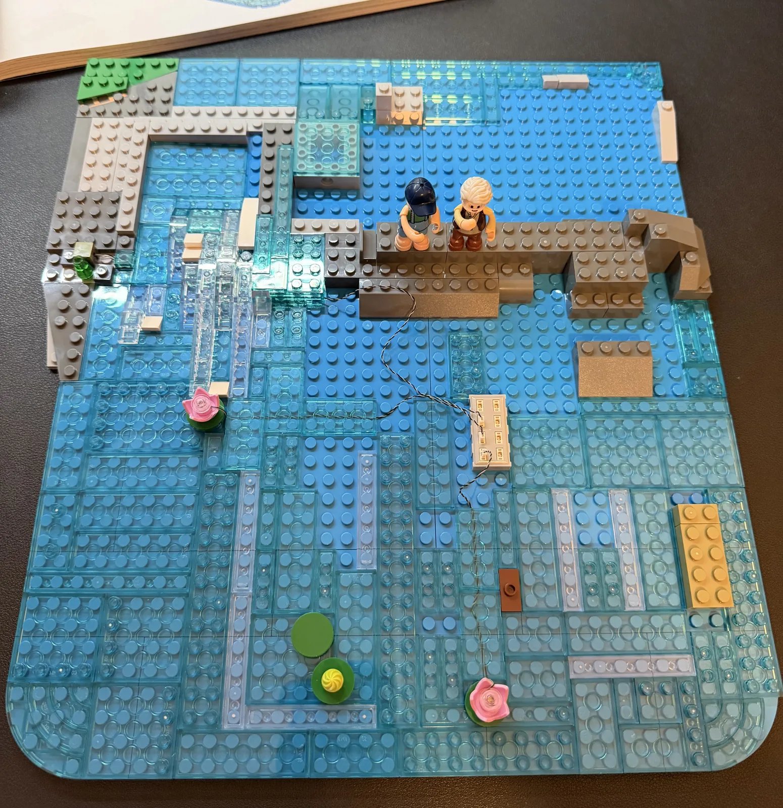 Lumibricks 10010 Waterfall Cabin — water base mid-build with LED block and both minifigures on the rock ledge