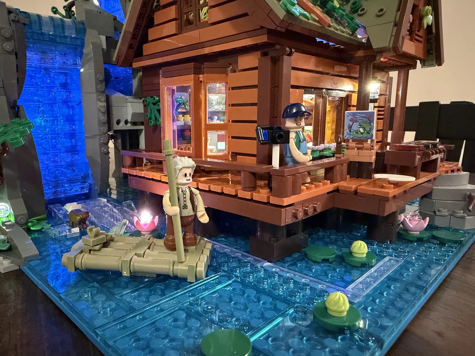 Lumibricks 10010 Waterfall Cabin — low-angle finished build with bear at the falls and artist on the deck