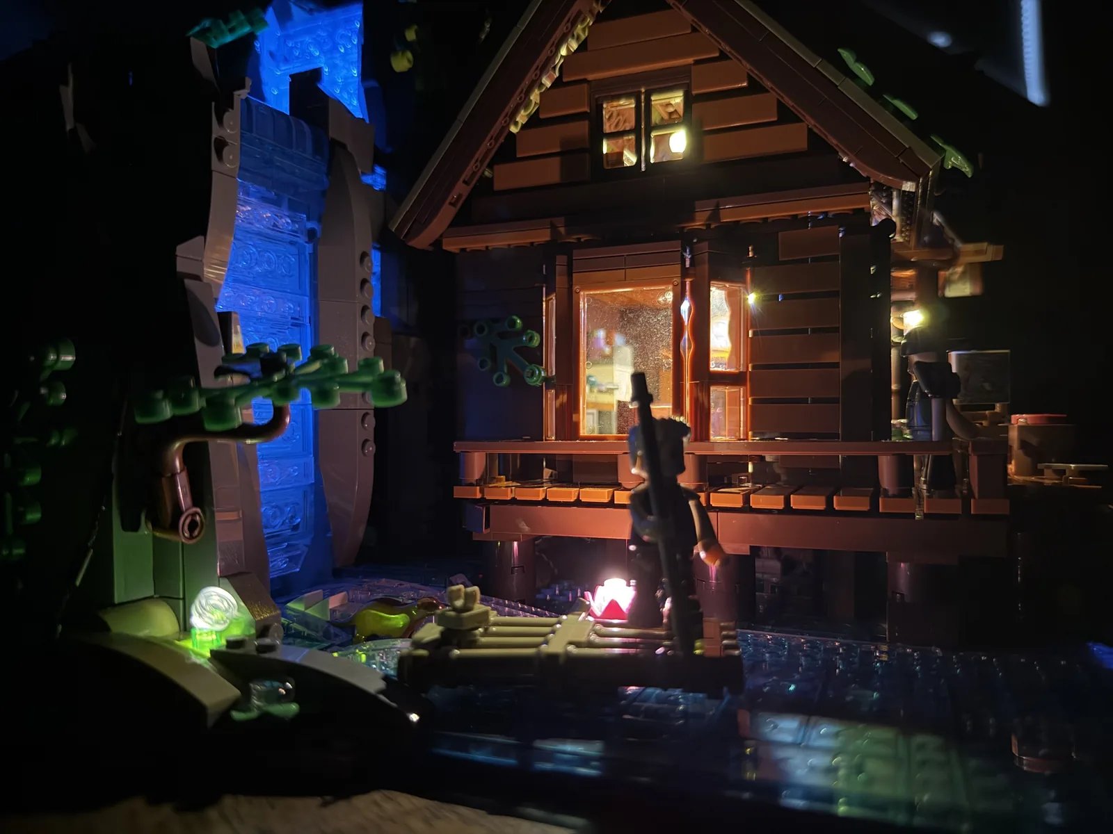 Lumibricks 10010 Waterfall Cabin — night high-angle with raft silhouette against the lit cabin