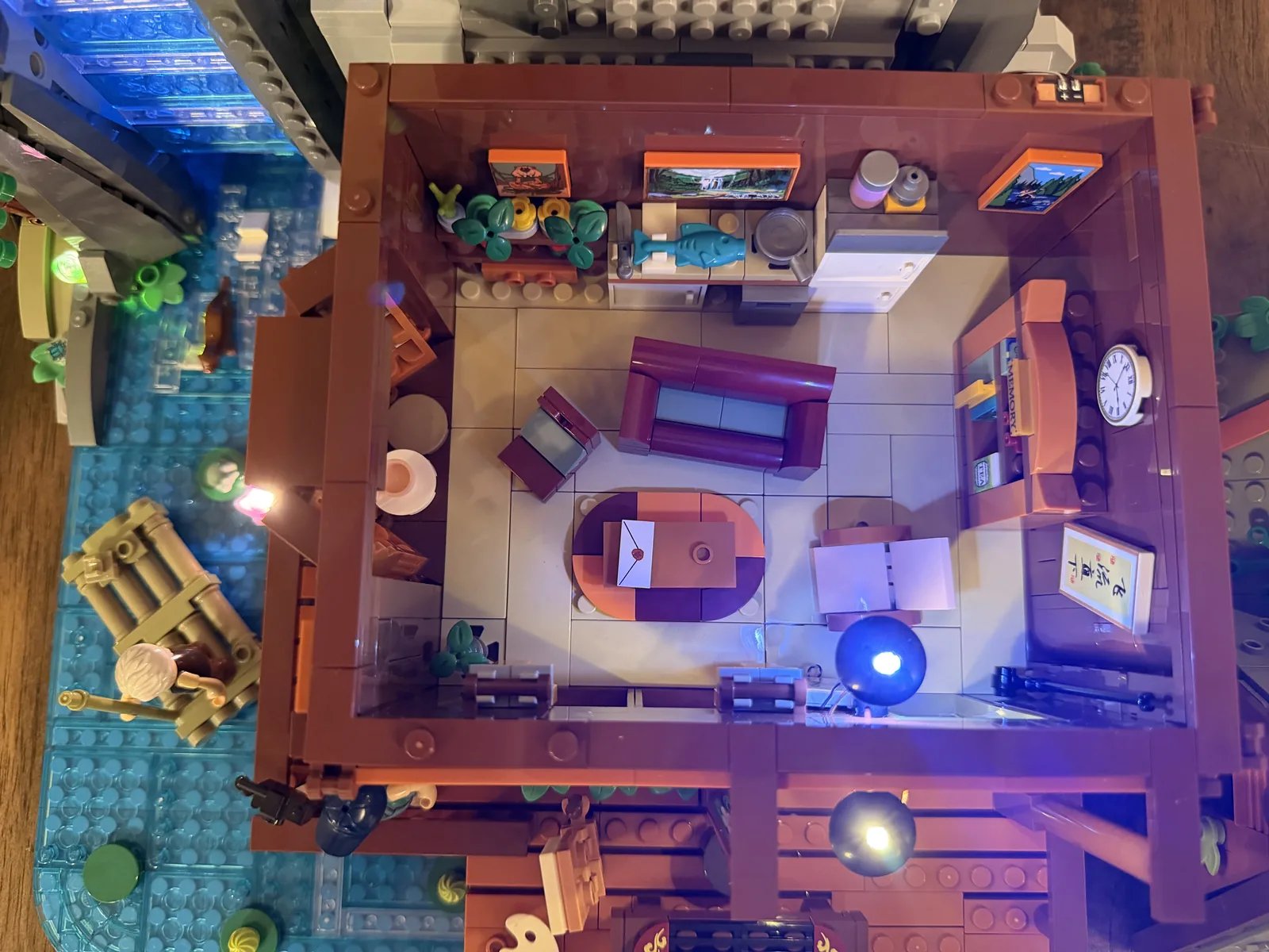 Lumibricks 10010 Waterfall Cabin — top-down first floor with warm LEDs, sofa and raft at the water's edge