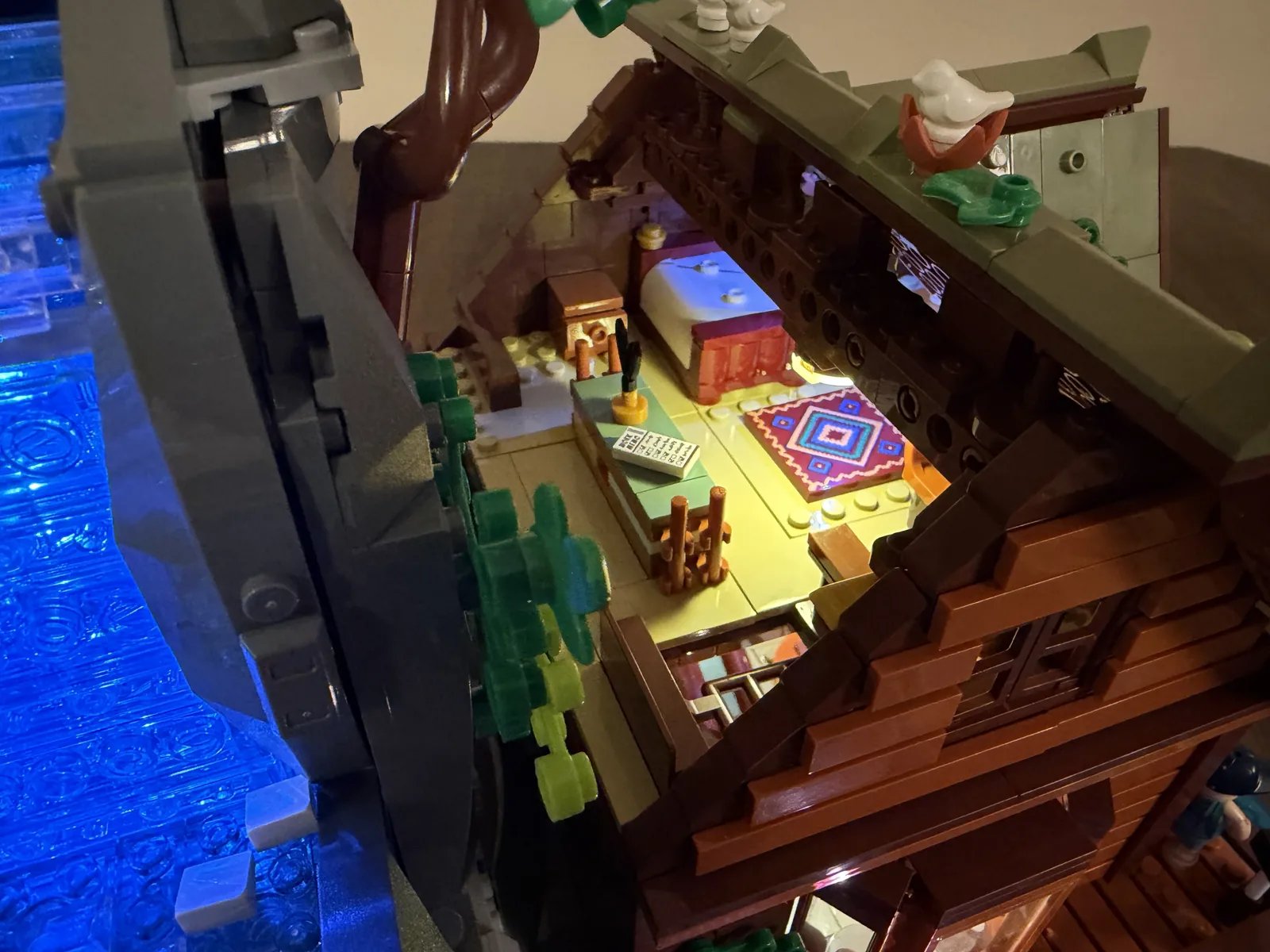 Lumibricks 10010 Waterfall Cabin — lit upper floor next to the glowing blue waterfall